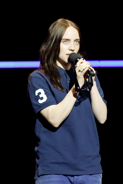 Billie Eilish talking into a microphone wearing a navy polo shirt